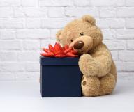 big teddy bear and blue square cardboard box with red bow on white brick wall background