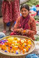 A young Nepali woman making flower garlands for religious offerings at Hindu temples in Kathmandu, Nepal