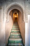 A person ascends the ornate staircase adorned with mosaic tiles in Fez\'s historical Cherratine Madrasa