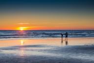 Two people standing on the shore, watching the sunset over Palmar Beach