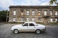 Car driving by a building on Abovyan Street where the windows are filled by black and white portraits of people; Gyumri, Shirak Province,