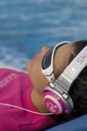 junge Frau mit Sonnenbrille liegt an einem Swimmingpool und hoert Musik mit einem Kopfhoerer | young woman with sunglasses and