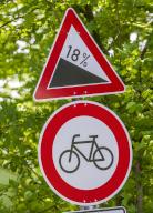 06 May 2024, Bavaria, Straßlach-Dingharting: Signs with the words "18 degree gradient" and "Passage prohibited for cyclists" can be seen on the side of the road near the Upper Bavarian municipality of Straßlach-Dingharting. The Bavarian Administrative Court did not reach a decision on Monday in the dispute over a ban on cycling downhill on a steep excursion route in Straßlach-Dingharting in Upper Bavaria. The case was brought by a cyclist from Munich. Photo: Peter Kneffel\/dpa