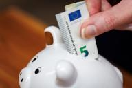 22 April 2024, Bavaria, Nuremberg: ILLUSTRATION - A woman throws a five-euro bill into a piggy bank. Photo: Daniel Karmann/dpa