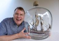 10 May 2024, Bavaria, Bad Kissingen: Matthias Schultz sits next to a 40-centimetre-high and 38-centimetre-long ship in a bottle that he built and which hangs in a 50-liter fermentation balloon. The model maker wants to enter the Guinness Book of Records with the "world