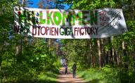 12 May 2024, Brandenburg, Grünheide: Activists from the "Stop Tesla" initiative have hung up a banner reading "Welcome to the Utopia Giga Factory No Cops, No Nazis, No Elon" in a forest near the Tesla Gigafactory Berlin-Brandenburg plant. According to the police, more than 1,000 activists marched from Fangschleuse station to the Tesla factory on Saturday. Photo: Patrick Pleul/dpa