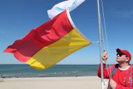 15 May 2024, Mecklenburg-Western Pomerania, Rostock: Lukas Knaup from the DRK water rescue service hoists the red and yellow flag on the rescue tower on the Baltic Sea beach in Warnemünde, signaling that this section of the beach is guarded by lifeguards. The water rescue service started the new season on the Baltic Sea beaches of Rostock on 09.05.2024. Photo: Bernd Wüstneck/dpa