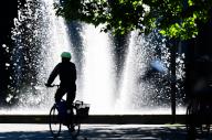 15 May 2024, Lower Saxony, Brunswick: A cyclist cycles in the sunshine in front of a fountain on Schlossplatz. Photo: Julian Stratenschulte/dpa