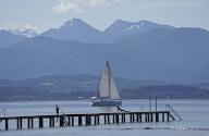 20 May 2024, Seebruck: A sailing boat passes a jetty in sunny weather on Lake Chiemsee in Upper Bavaria. Photo: Uwe Lein/dpa