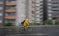 22 May 2024, Berlin: A cyclist wearing a yellow rain jacket rides across the road during a shower. Photo: Sebastian Gollnow/dpa