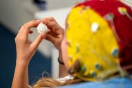 29 April 2024, Thuringia, Jena: An EEG subject wears an EEG cap with electrodes for EEG measurement and holds a model of a brain in her hand. On July 6, 2024, electroencephalography (EEG), which was first tested on humans in Jena, will celebrate its 100th anniversary. The procedure measures the electrical activity of the brain and displays it graphically. Photo: Jacob Schröter/dpa