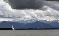 30 May 2024, Bavaria, Possenhofen: A sailing boat is sailing on Lake Starnberg while thunderclouds pass over the Alps. Photo: Katrin Requadt/dpa