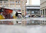 30 May 2024, Berlin: The surrounding buildings and passers-by are reflected in a puddle on Berlin