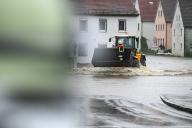 01 June 2024, Bavaria, Fischach: A firefighter stands on the shovel of a tractor driving through a flooded road. After the heavy rainfall of the last few days, there is flooding in the region. Photo: Marius Bulling/dpa