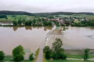02 June 2024, Bavaria, Kammeltal: A car drives over a road partially flooded by the Kammel river in the direction of the district of Hammerstetten (aerial view with a drone). Photo: Karl-Josef Hildenbrand/dpa