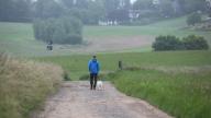 02 June 2024, North Rhine-Westphalia, Bergisch Gladbach: A man is walking a dog along a country lane in cloudy weather. Photo: Sascha Thelen/dpa