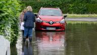 03 June 2024, Bavaria, Baar-Ebenhausen: Two women are talking on a flooded street in their neighborhood. Photo: Peter Kneffel/dpa - ATTENTION: The license plate number of the car has been pixelated for legal reasons