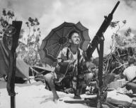 U.S. Coast Guard invader of Saipan is out of uniform. Wearing a silk kimono under the shade of a pastel parasol, he takes aim on a parakeet with a captured Jap gun. Ca. June 1944. Northern Mariana Islands, World War 2. (BSLOC_2014_10_107)
