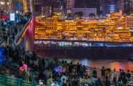 Tourists walk on a bridge overlooking the illuminated Hongyadong cluster of traditional looking buildings in southwest China\'s Chongqing Municipality Friday, May 03, 2024