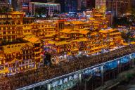 Tourists walk on a bridge beside the illuminated Hongyadong cluster of traditional looking buildings in southwest China\'s Chongqing Municipality Friday, May 03, 2024