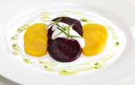 Sliced yellow and purple beets with chives and crème fraiche, drizzled with olive oil on white plate