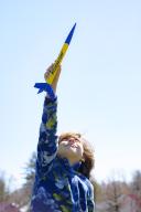 Young boy holding a yellow and blue toy rocket in air against blue sky