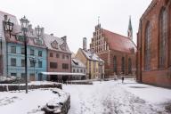 Snow-covered medieval houses stand in the street of butchers, Skarnu Iela, with St Johns Church on the right. oldest church in Riga, Latvia