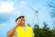 Worker wearing safety gear talking to the mobile phone in a wind energy