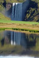 Water masses plunge vertically into the depths, reflection in the water, green landscape, Skogafoss, Iceland