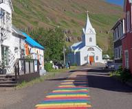 Small church and houses line a street decorated with rainbow colours, Seydisfjördur
