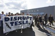 Participants with banner Disrupt Tesla in front of the Tesla Gigafactory at the demonstration Water. Forest. Justice against the expansion of the Tesla Gigafactory in Grünheide near Berlin, 11.05