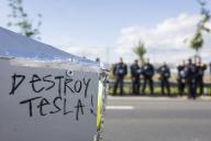 Destroy Tesla! slogan on a cardboard Cybertruck model in front of the factory premises guarded by police officers at the Water. Forest. Justice against the expansion of the Tesla Gigafactory in Grünheide near Berlin, 11 May