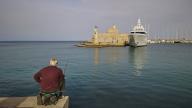A man fishing on a shore with a view of an old fortress and a luxury yacht at sunset, Fort of Saint Nikolaos, harbour area, Rhodes Town, Rhodes, Dodecanese, Greek Islands, Greece