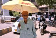 HYDERABAD, PAKISTAN, MAY 18: Commuter holds an umbrella over his head to save themselves from scorching sun pass through a road during hot day of summer season, in Hyderabad on Saturday, May 18, 2024. (Sajjad Zaidi/PPI Images
