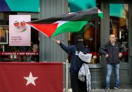 A protester stands outside Pret A Manger with a Palestinian flag and a placard reading 
