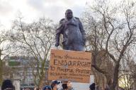 A protester holds up a placard next to the Winston Churchill statue during the demonstration. Crowds of people gathered in London to protest against the heavy-handed response by the police at the Sarah Everard vigil, as well as the government