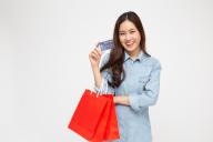 Portrait of smiling asian women wearing blue jean shirt holding credit card and red shopping bag isolated over white background, Young woman looking at camera, Happy feeling of shopper concept
