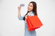 Portrait of smiling asian women wearing blue jean shirt holding credit card and red shopping bag isolated over white background, Young woman looking at camera, Happy feeling of shopper concept