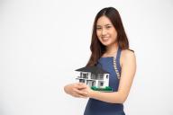 Young Asian woman smiling and hugging dream house sample model isolated over white background, Real estate and home insurance concept