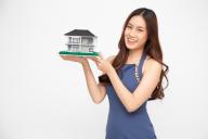 Young Asian woman smiling and holding house sample model isolated over white background, Real estate and home insurance concept