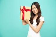 Happy beautiful asian woman smile with gold gift box isolated on light green background. Teenage girls in love, Receiving gifts from lovers. New Year, Christmas and Valentines Day concept