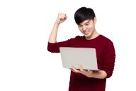 Excited Asian man looking at laptop computer screen and raising his arm up with celebrating success isolated over white background