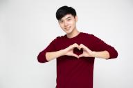 Portrait of happy Asian man making heart with fingers isolated on white background