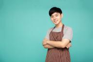 Portrait of Asian workers fresh market with brown apron standing with arms crossed isolated on green background
