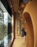 A visitor snaps a picture through a large window. Seating pod in the foreground, timber cladding and copper window frame details. The Beezantium at The Newt, Bruton, United Kingdom. Architect: Invisible Studio, 2021