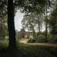 The apiary pavilion seen between the trees with a path winding towards it. The Beezantium at The Newt, Bruton, United Kingdom. Architect: Invisible Studio, 2021