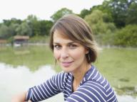 Germany, Munich, Mature woman sitting beside lake, smiling, portrait NO sales in France until 2021