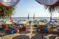 Indonesia, Bali, Denpasar, Tourists under colorful sunshades at Kuta beach